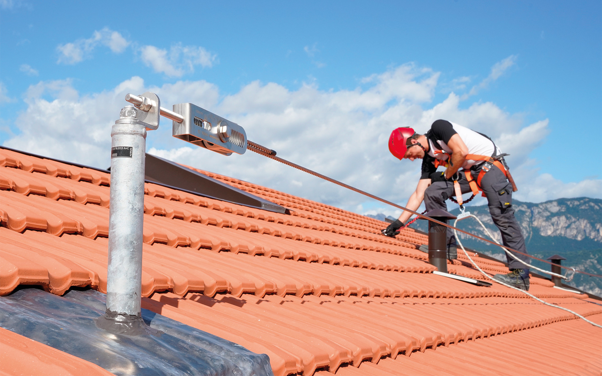 Worker using permanent fall protection system on sloped roof with lifeline and certified anchorage point for construction site safety