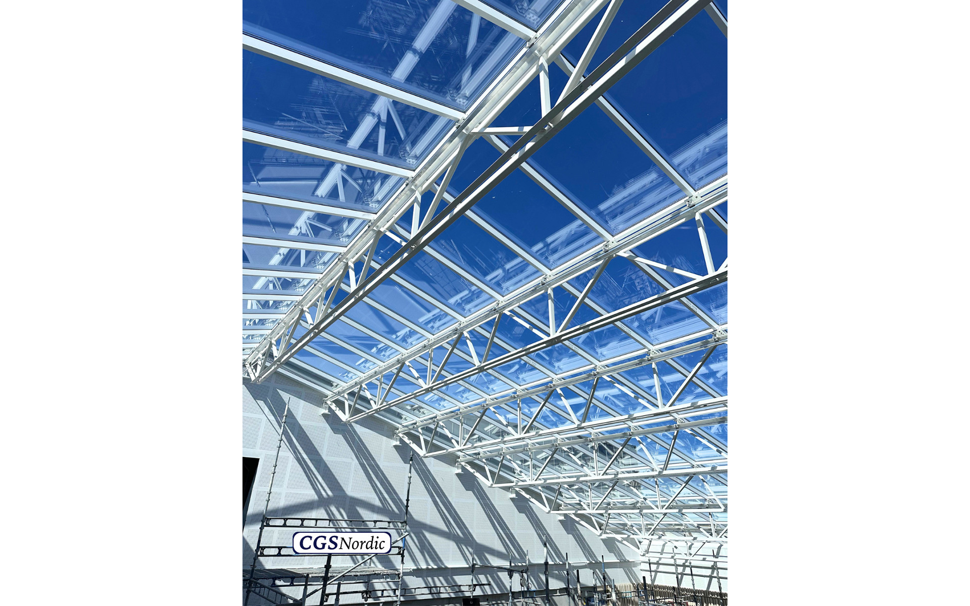 CGS Nordic technician wearing a white safety helmet and gloves, preparing H-RAIL rail components before installation in a glazed building atrium.